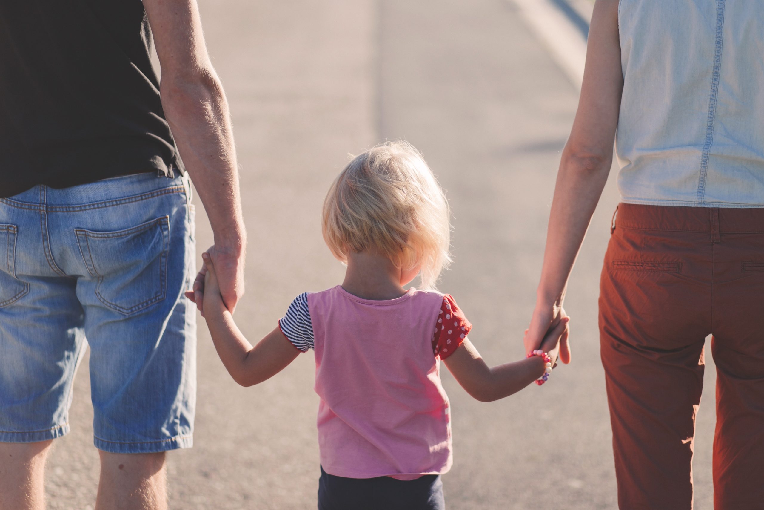 a young child holding the hands of both parents